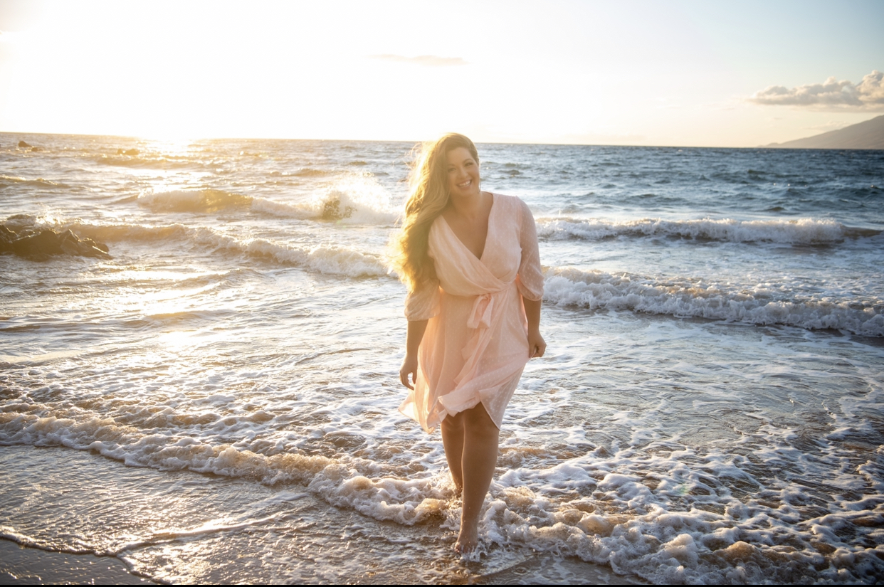Amy McNally walking barefoot through shallow ocean surf at sunset